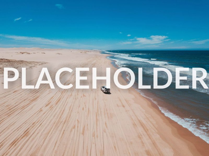 Aerial shot of a 4-wheel drive driving along a white sand beach.